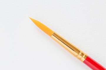 Naklejka premium round paint brush laying on blank sheet of watercolor paper