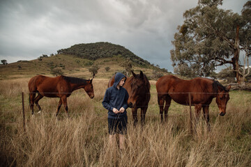 Teen boy standing at farm fence interacting with horses