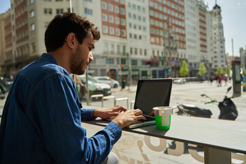 man sipping a hot drink at a bar while using his laptop to work or study