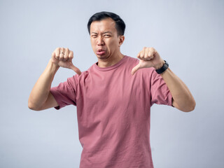A man in a pink shirt shows a thumbs-down gesture with a displeased expression, sticking out his...