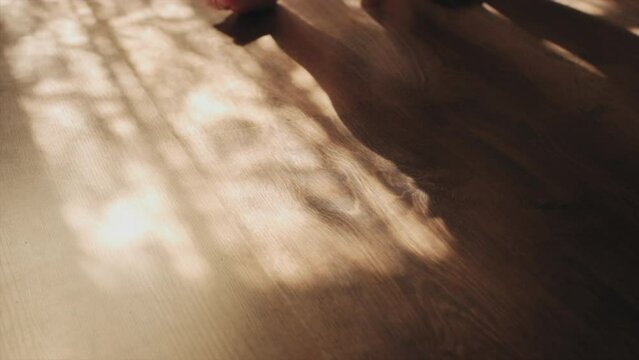 Unknown caring young mother and infant child. Childhood concept. Selective focus of little feet walking on floor. Close-up of baby learning to walk at home. Baby first steps