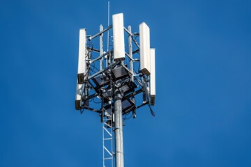 A tall metal tower with a ladder and multiple white antennas stands against a bright blue sky.