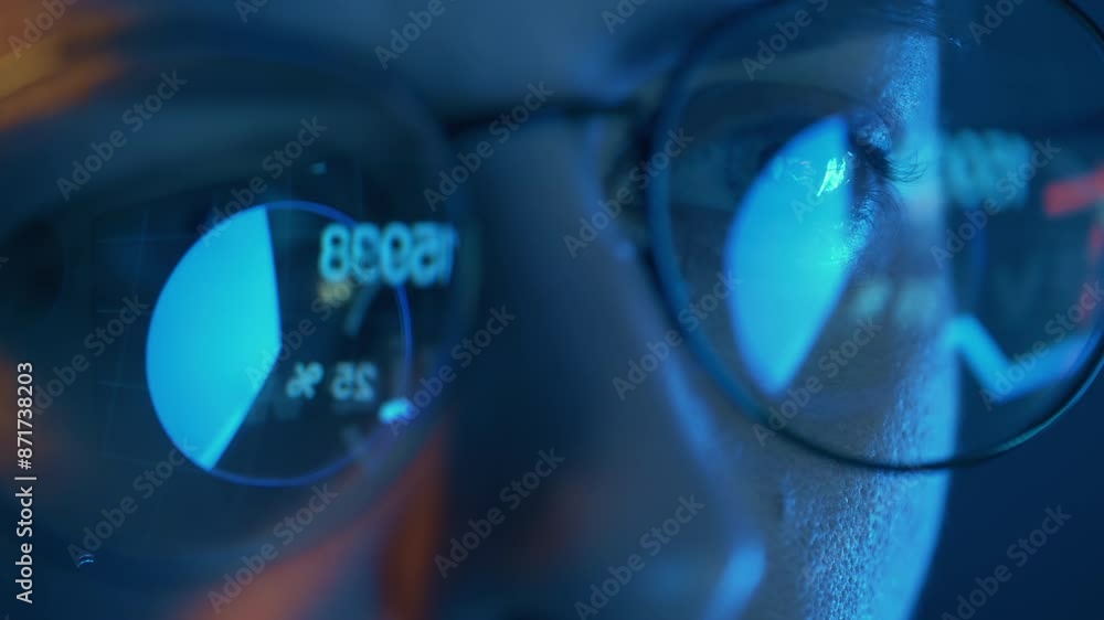 Poster trader wearing glasses is working on laptop computer. reflection of screen with stock market charts.