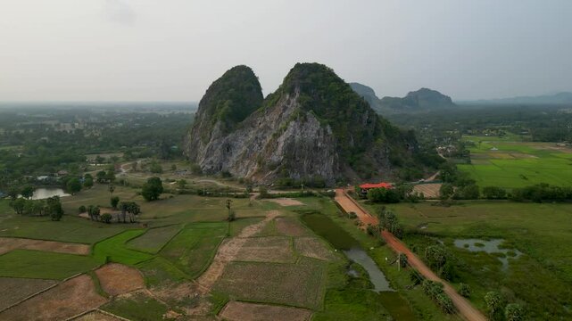 Drone shot of farmland and individual mountains rising out of it. Rice fields. The setting sun, greenery, buildings and gravel red Cambodian roads. Kampot. Cambodia.