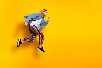 Full length photo of handsome young male running fast have fun dressed stylish denim garment isolated on yellow color background
