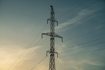 High voltage pole and wires against blue sky and setting sun.