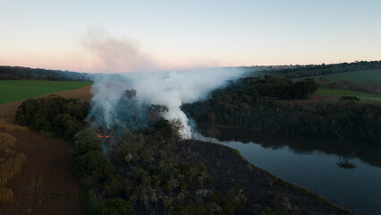 Smoke in the air near the lake and vegetation. Forest fire in the dry season in the rural area of ​​Apucarana with trees being burned.