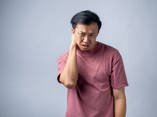 Fototapeta premium A man in a pink shirt holds his neck with a pained expression, indicating discomfort or neck pain. The plain light blue background emphasizes his distress and highlights