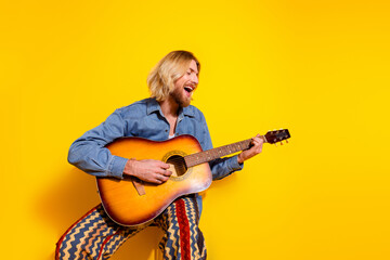 Photo portrait of attractive young man play guitar singing dressed stylish denim clothes isolated on yellow color background
