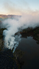 Smoke in the air near the lake and vegetation. Forest fire in the dry season in the rural area of ​​Apucarana with trees being burned.