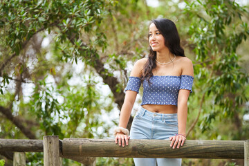 A woman wearing a blue shirt and jeans is standing on a wooden fence