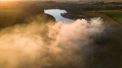 Smoke in the air near the lake and vegetation in the morning light. Forest fire during a dry period in the rural area of ​​Apucarana with burning trees.