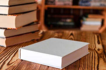 Fototapeta premium Books. A white notebook with space for text lies on a wooden table against the background of bookshelves