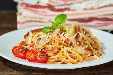 Pasta with bacon in the foreground. There is a piece of bacon in the background. Meat production