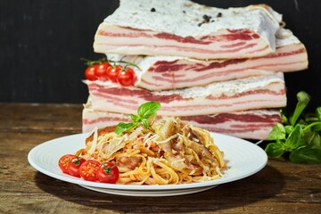 Pasta with bacon in the foreground. There is a piece of bacon in the background. Meat production
