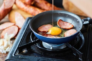 Step-by-step cooking of the dish. Pieces of sausage and eggs are fried in a frying pan on a camp stove.