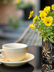 Cup of coffee standing on table with yellow pansy flowers in outdoor cafe