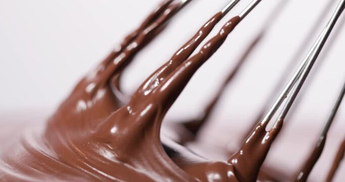 A close-up capture of a whisk with dripping chocolate against a white background, suitable for baking themes