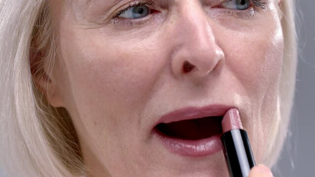 Close-up portrait of Old woman uses lipstick or a pomade. Senior female applies make up or cosmetics to the lips. Facial skin care in old age. Mature elderly lady. Concept of natural beauty.