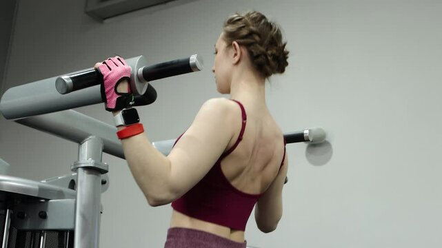 Young athletic woman doing pull-ups on a machine in the gym. Smooth camera movement, selective focus.