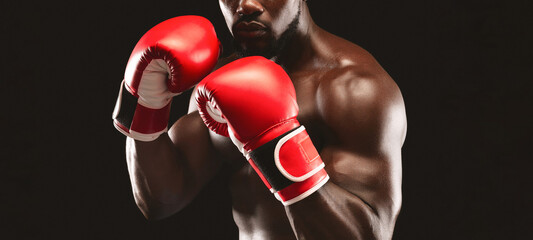 A close-up shot of a boxer wearing red boxing gloves against a black background. The boxer is...