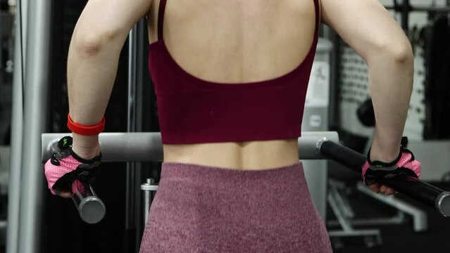 Young athletic woman doing exercise for training triceps dips on parallel bars in the gym, selective focus, camera movement.