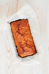 Delicious freshly baked homemade loaf cake in a pan, top view on white wooden background, flat lay style. Healthy sweet food.