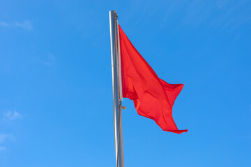 Red flag is waving against blue sky