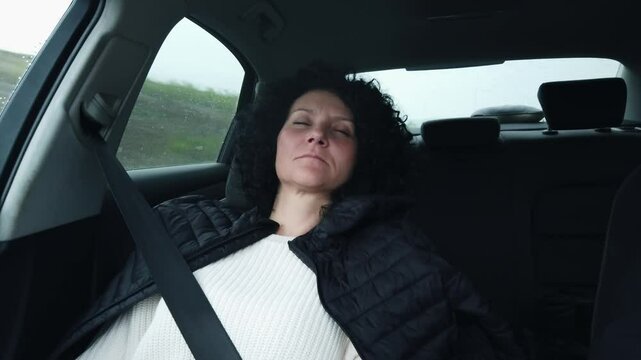 Hispanic woman with curly hair is sleeping in traveling car driving on highway with rain drops on glass at background
