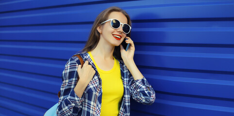 Happy young woman calling on phone, girl talking on the smartphone looks away on blue background