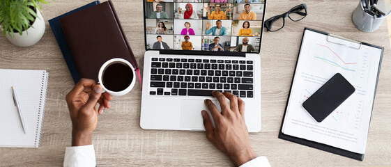 A person is sitting at a desk in an office setting, working on a laptop while participating in a video conference call. They are holding a cup of coffee in their left hand, web-banner