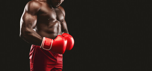A muscular boxer stands with his fists clenched in red boxing gloves, ready for a fight.