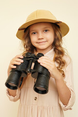 Traveler child. Child discoverer. Young researcher. Little girl in a safari hat with binoculars in her hands. Concept: search for adventure and treasure. Cute happy girl in safari clothes