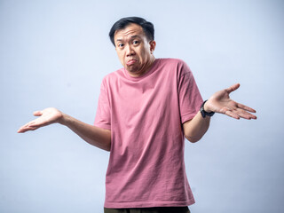 An Asian man in a pink shirt shrugs with a confused and uncertain expression, his arms outstretched...