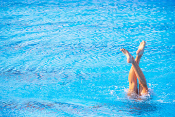Female swimmer legs point up out of the water in swimming pool with copy space