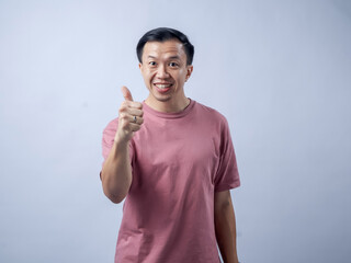 A man in a pink shirt smiles and gives a thumbs-up gesture, exuding positivity and approval. The plain light blue background highlights his cheerful and confident demeanor.