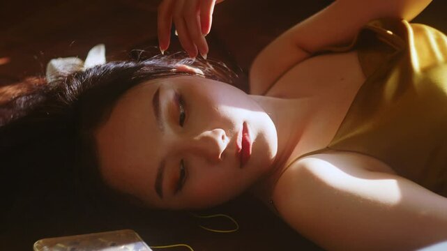 female Chinese young attractive model touching her skin fafe with long nails fingers while laid on the sunshine in her room 