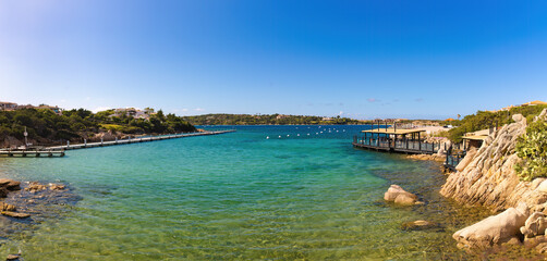 Panorámica de Porto Cervo en Cerdeña, Italia, en un día despejado. El mar de color verde y azul se extiende hacia un muelle al fondo.