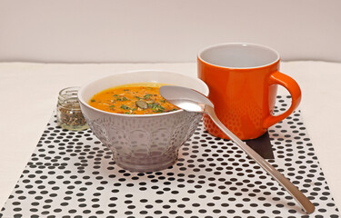 Pumpkin Soup in Bowl With Spoon Served With Mug at Table