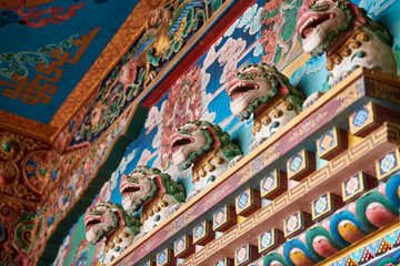 Fototapeta premium Snow lions with turquoise manes bas reliefs on wall above entrance to Buddhist temple, decorative and religious decoration of ancient temple facade, snow lions mythological celestial animal of Tibet