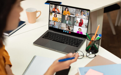 This image shows a woman sitting at a desk, participating in a video conference meeting on her...