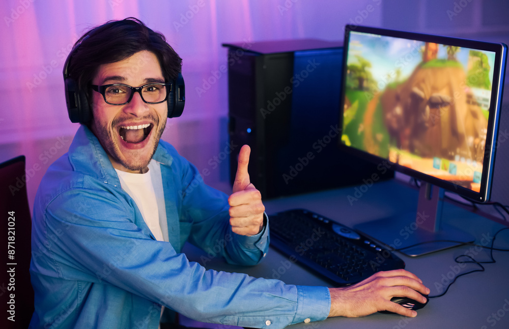 Poster a young man wearing headphones sits in front of a computer, playing a video game. he is smiling and 