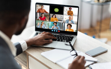 African American businessman sits at his desk and participates in a video conference meeting on his laptop. He is listening intently to the speakers on the screen