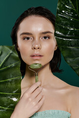 A woman uses a jade roller on her face against a vibrant green backdrop. © LIGHTFIELD STUDIOS