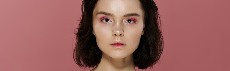 A woman poses against a pink backdrop, her gaze direct and captivating.
