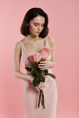 A woman in a pink dress holds a bouquet of roses in front of a bright pink background.