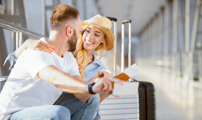 Loving couple in airport using travel app on smartphone, waiting for departure, panorama with copy...