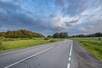 A road with a few trees in the background and a cloudy sky