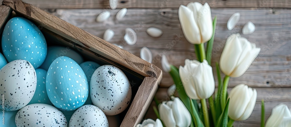 Poster colorful easter eggs in blue and white hues alongside white tulips placed in a wooden box, creating 