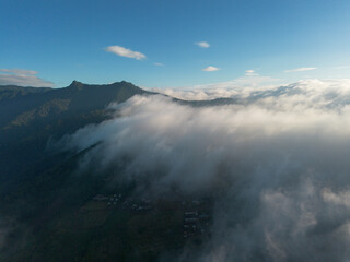 A high-angle landscape, a village in the middle of mountains surrounded by white fog. Beautiful landscapes, villages in the middle of forests, green mountains, clear skies. Photos from a drone